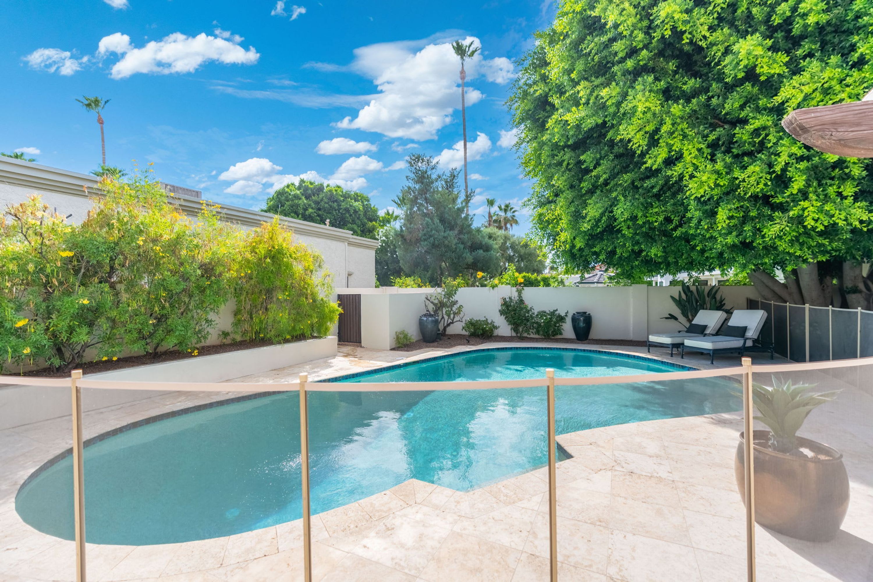 A swimming pool with a curved edge, surrounded by a fence, and a seating area with lounge chairs.