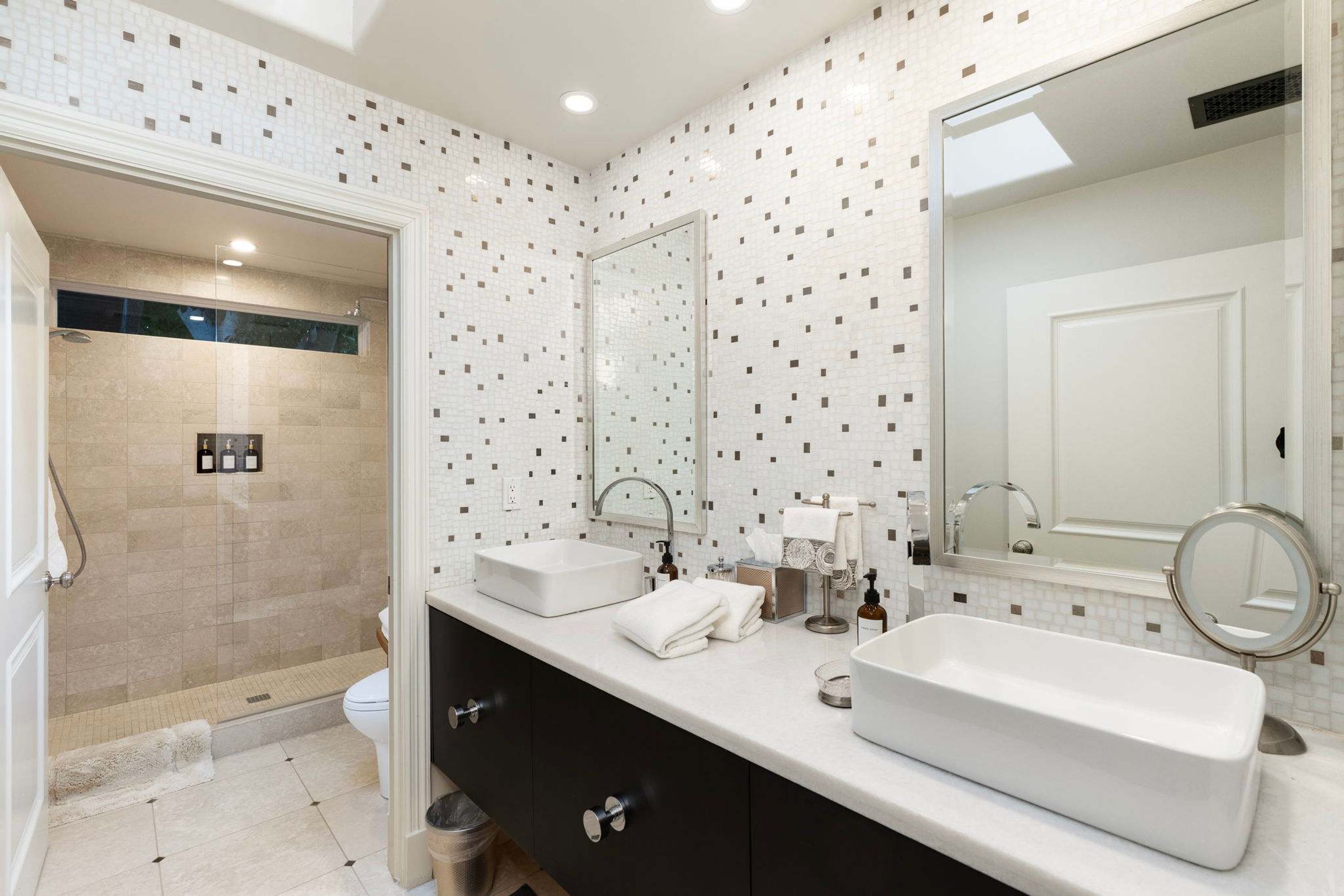 A bathroom with two sinks, a large mirror, and a shower area.
