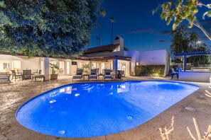 Ein Swimmingpool mit Liegestühlen, eine überdachte Terrasse und ein Gebäude mit weißer Fassade.