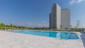 En swimmingpool med solstolar och en hög byggnad i bakgrunden.