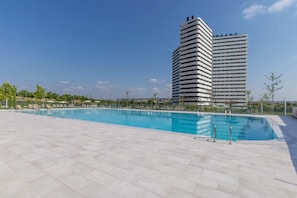 Una piscina con sillas de descanso y un edificio alto al fondo.