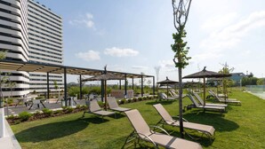 En takterrass med en loungeyta, solstolar, parasoller och utsikt över en modern byggnad.