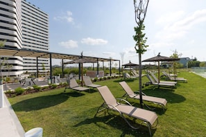 Un área de lounge en la azotea con sillones de sol, sombrillas y vistas a un edificio moderno.