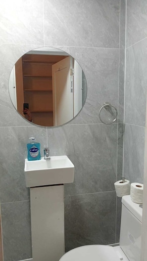 Ein Badezimmer mit einem weißen Waschbecken, einem runden Spiegel, einer Toilette und einem Handtuchhalter.