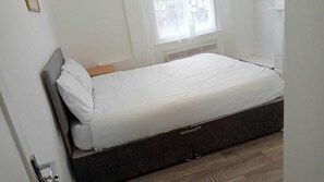 A single bed with a dark headboard in a room with white walls and a window with sheer curtains. - The Shepherd Bush Stay in London by Gndj (London)