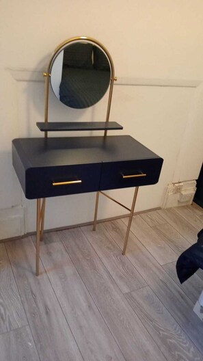 Un bureau noir avec des pieds dorés et un miroir rond.