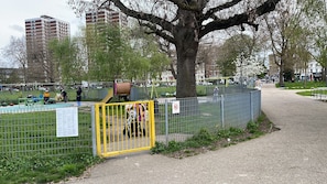 Ein eingezäunter Parkbereich mit Spielgeräten, einem Baum und einem Weg.