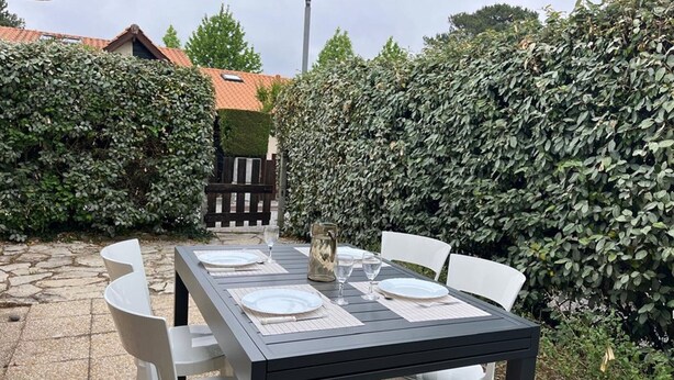 A patio table set with white chairs, a glass pitcher, and plates.