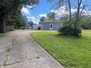 A residential area with a concrete pathway, a small house, and a grassy yard.