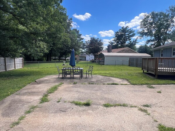 A backyard with a patio table and chairs, a wooden deck, and a house in the background.