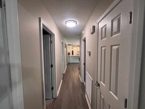 A hallway with white doors, a ceiling light, and a kitchen area in the distance.