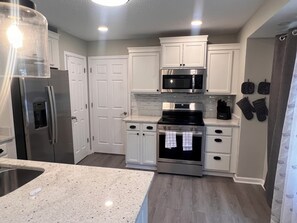 A modern kitchen with white cabinets, stainless steel appliances, a granite countertop, and a wooden floor.