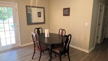 A dining area with a round table, four chairs, a mirror, and two framed pictures on the wall.