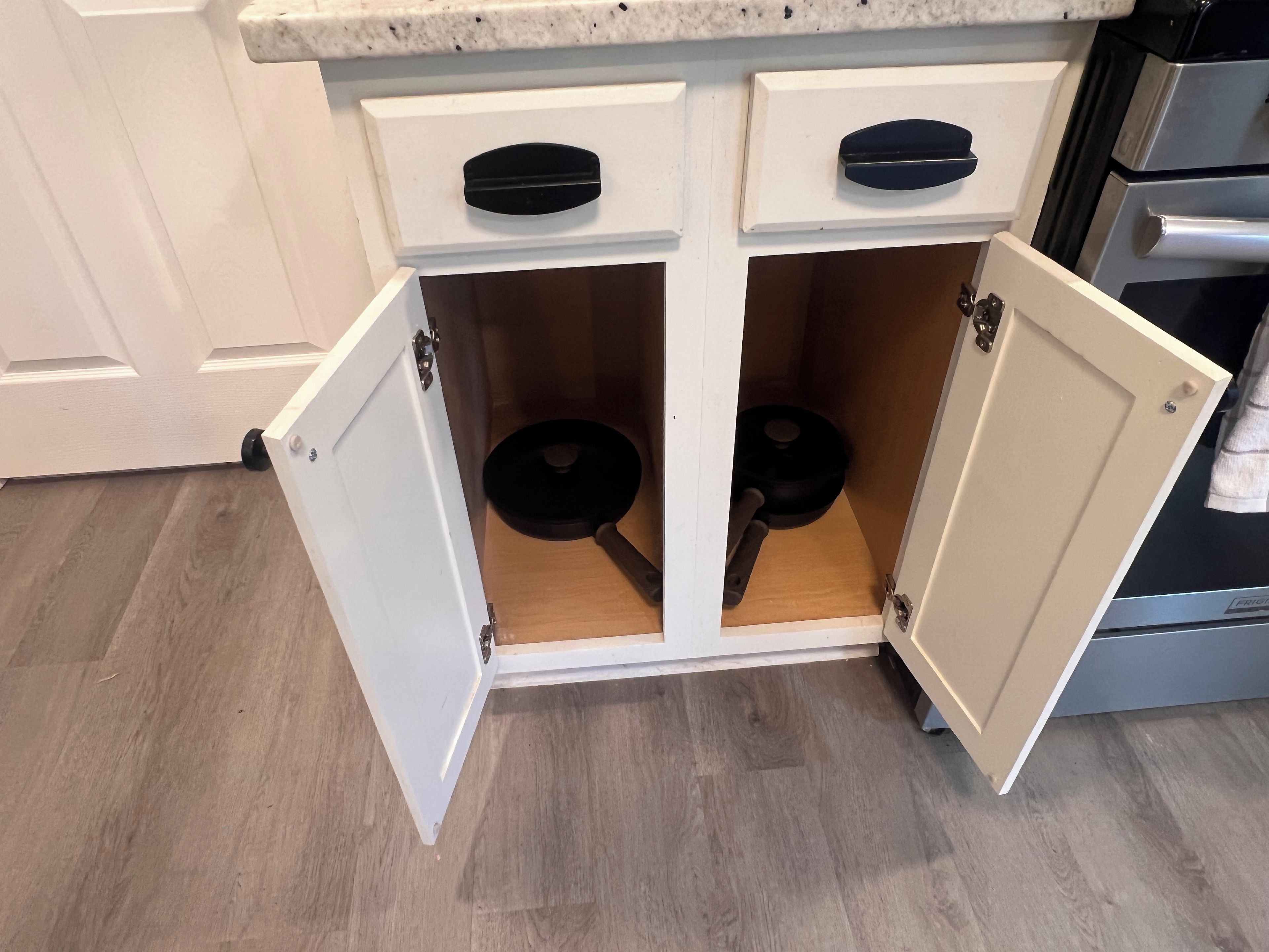 A kitchen with white cabinets, two black handles, and a wooden floor.