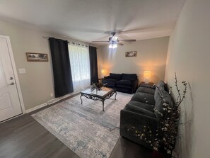 A living room with a ceiling fan, a sofa, a coffee table, and a lamp.