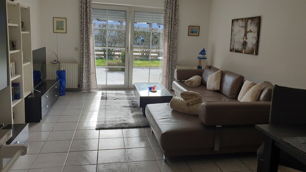 Ein Wohnzimmer mit einer Couch, einem Fernseher und Blick durch eine Glastür.