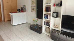 Ein Wohnzimmer mit einem weißen Schrank, einem Bücherregal, einem Fernsehschrank und einer Kaffeemaschine.