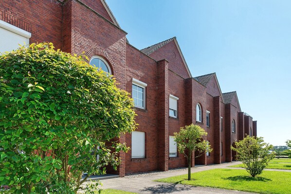 A red brick building with multiple windows and a well-maintained lawn. - Holiday Apartment “Vacation at Haus Borkum” with Balcony and Wi-Fi (Dornum)