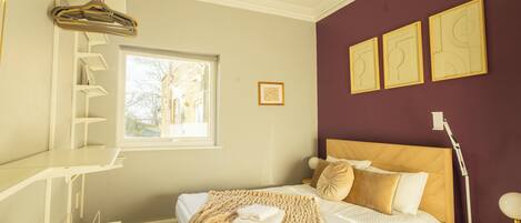 Ein Schlafzimmer mit Bett, Fenster, Nachttisch und einer an der Wand befestigten Ablagefläche.