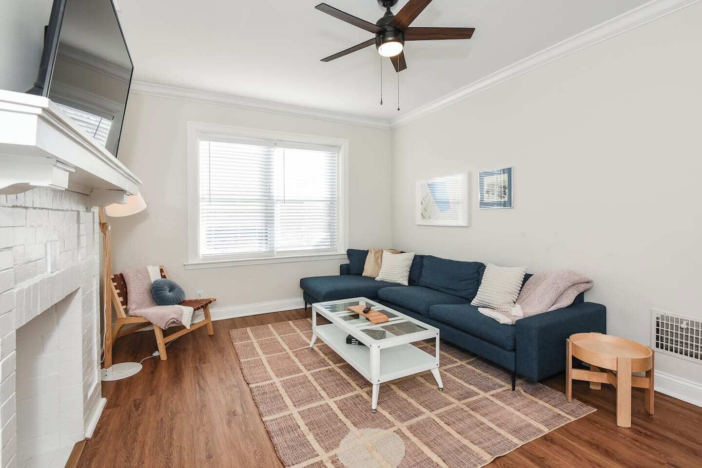 A living room with a fireplace, a blue sofa, a coffee table, and a ceiling fan.