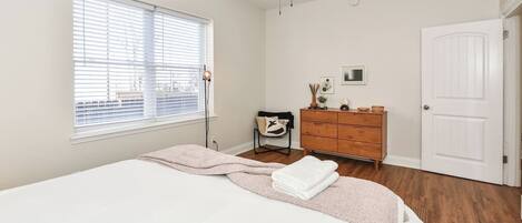 Ein Schlafzimmer mit Bett, Schminktisch, Stuhl, Fenster mit Jalousien, Deckenventilator und Tür.