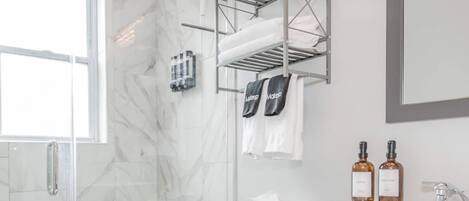 Een badkamer met een glazen douchecabine, een wit toilet, een wastafel met spiegel en twee flesjes lotion op het aanrecht.
