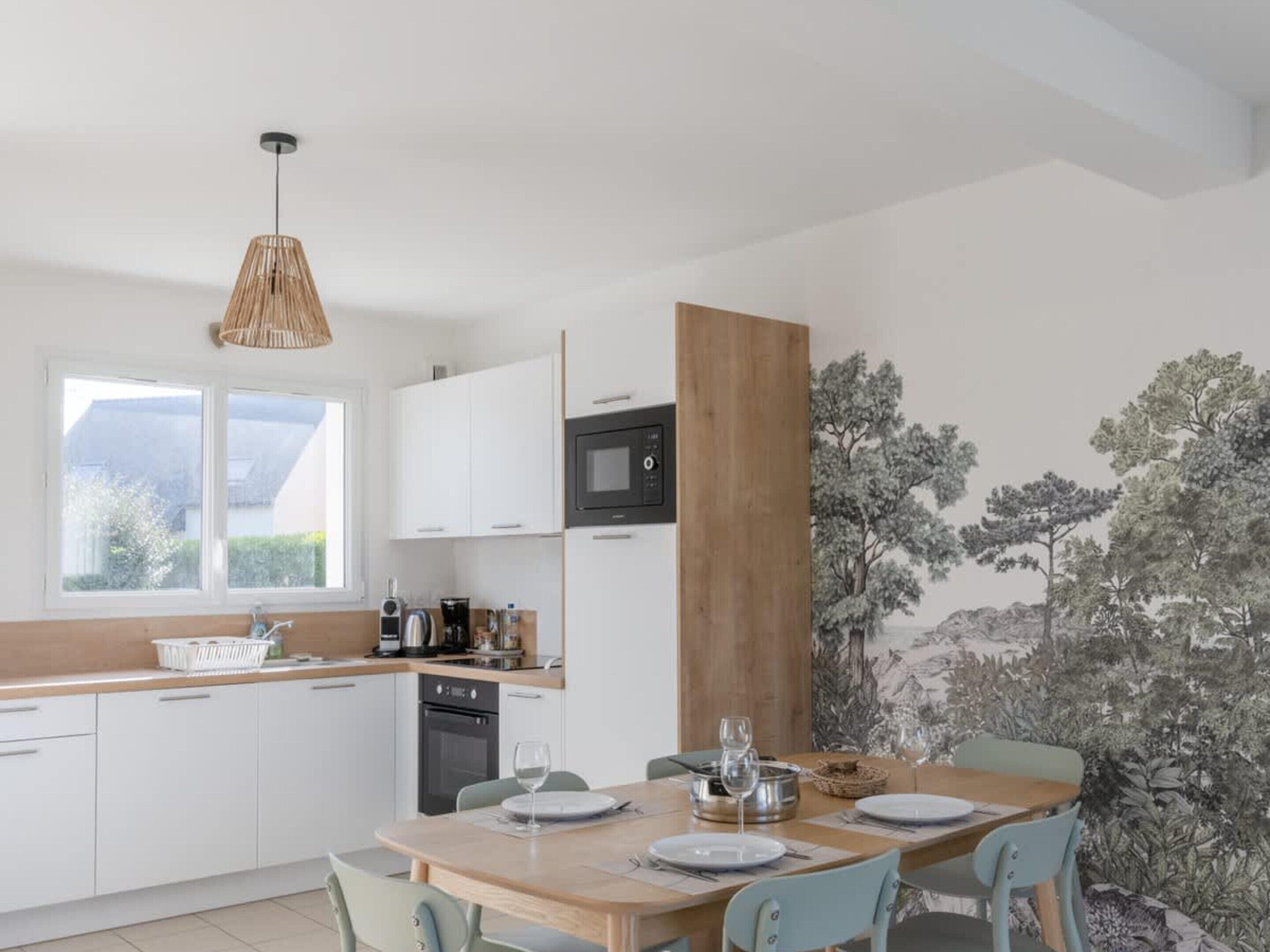A modern kitchen with white cabinets, a wooden dining table, and a large window.