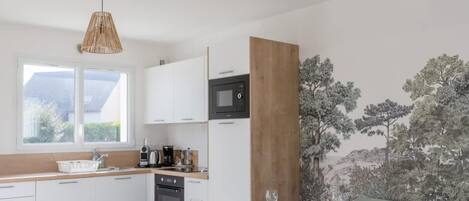 A modern kitchen with white cabinets, a wooden dining table, and a large window.