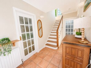 A staircase leading to a second floor, a wooden cabinet with a lamp, and a door with frosted glass panels. - Ashwood Stays
Where Comfort Meets Elegance,Your Comfortable Home Away From Home (Chessington)