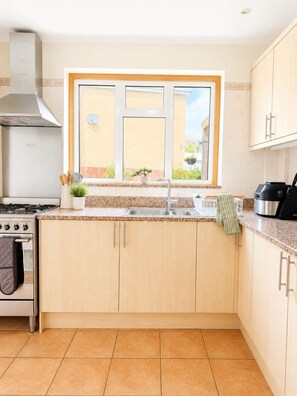 A kitchen with a gas stove, oven, stainless steel sink, and wooden cabinets. - Ashwood Stays
Where Comfort Meets Elegance,Your Comfortable Home Away From Home (Chessington)
