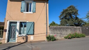 Un bâtiment à deux étages, doté d’une façade beige, d’une porte bleue avec une grille en métal et d’une fenêtre avec des volets bleus.