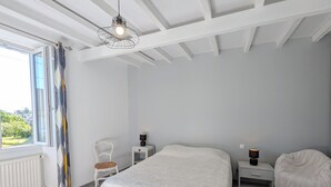 Une chambre à coucher avec un grand lit, une chaise, des tables de chevet, un luminaire suspendu et une fenêtre avec des rideaux.