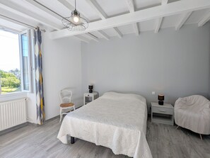 Ein Schlafzimmer mit einem großen Bett, einem Sessel, Nachttischen, einer Pendelleuchte und einem Fenster mit Vorhängen.