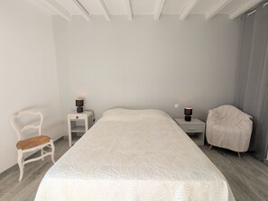 Ein Schlafzimmer mit einem großen Bett, zwei Nachttischen mit Lampen, einem Sessel und einem Fenster mit Vorhängen.