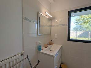 Ein Badezimmer mit Waschbecken, Spiegel und einem Fenster mit Blick auf Grünflächen.
