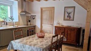 Uma sala de jantar com uma mesa posta para quatro pessoas, cadeiras de madeira, um candelabro, um armário de madeira e uma porta com uma pintura de um veado.