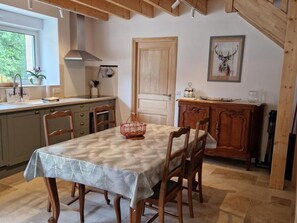 A dining area with a table set for four, wooden chairs, a chandelier, a wooden cabinet, and a door with a deer painting.