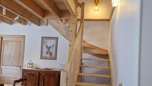 Uma escada de madeira leva a um quarto no sótão, com teto inclinado e uma luminária.