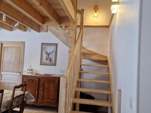 A wooden staircase leading to a loft bedroom with a sloped ceiling and a single light fixture.