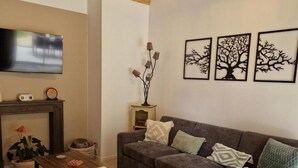 Uma sala de estar com sofá cinzento, mesa de centro de madeira, lareira e obras de arte na parede.