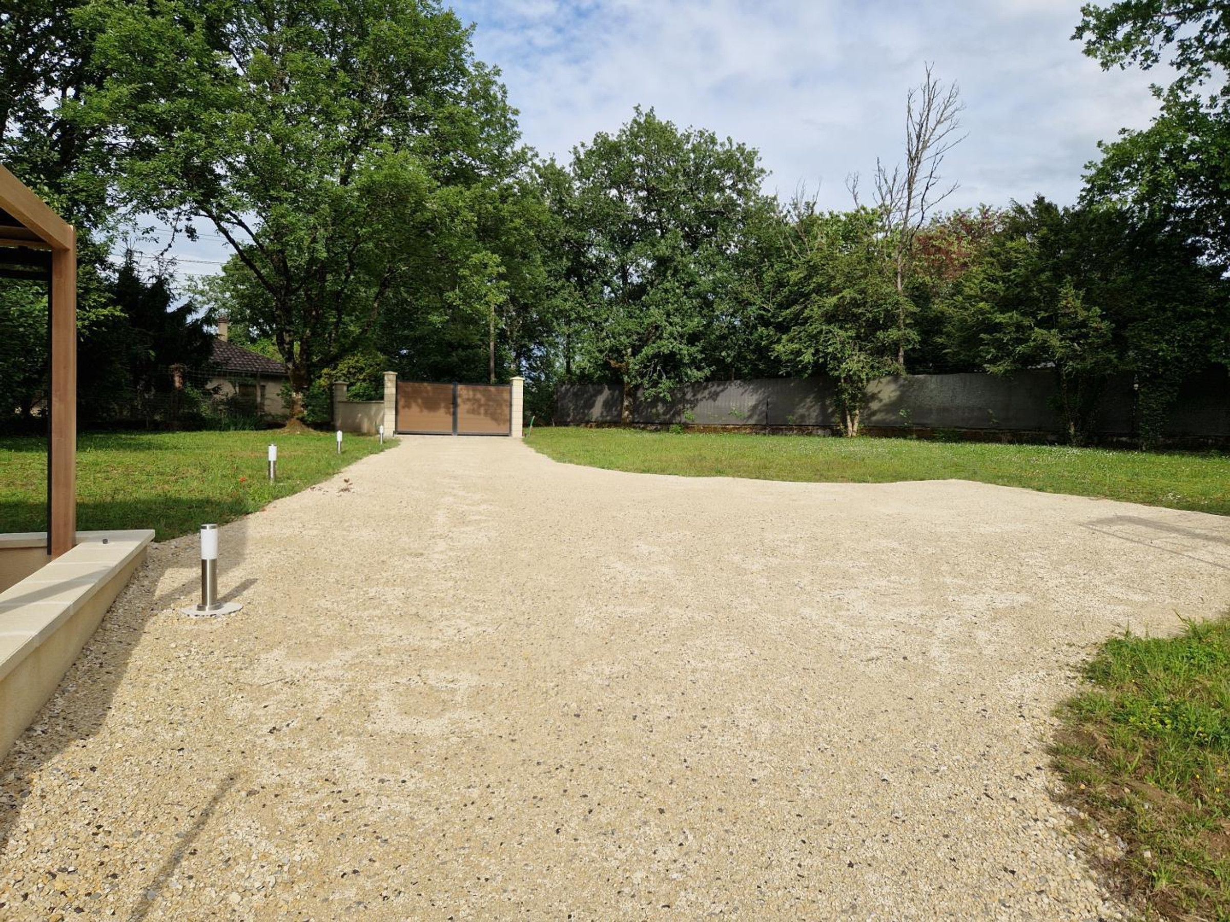 A gravel driveway leading to a gated entrance with a wooden structure on the left.