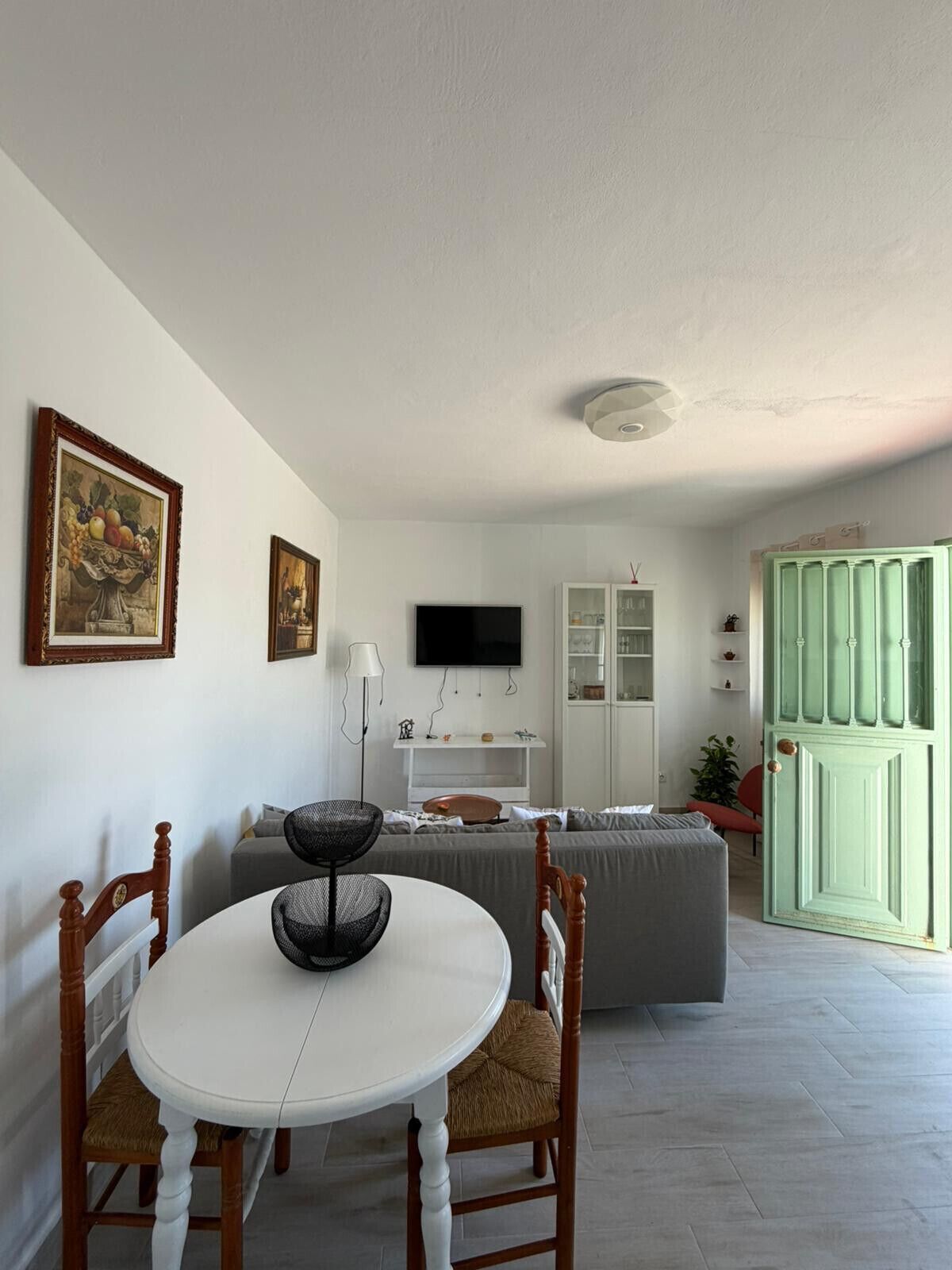 A living room with a white round table, two chairs, a sofa, a television, and a green door.