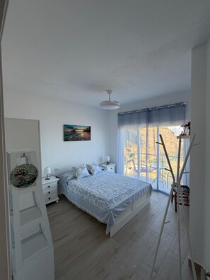 Een slaapkamer met een bed, nachtkastjes, een schilderij, een raam met gordijnen en uitzicht op de omgeving.