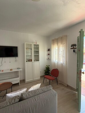 A living room with a TV, white cabinets, a red chair, a sofa, and a door. - A&N Playa Madrid 1, Almayate (Vélez Málaga)