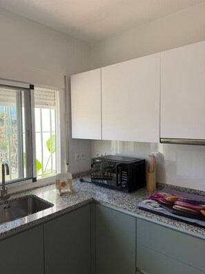 A kitchen with white cabinets, a microwave, a sink, and a window with blinds. - A&N Playa Madrid 1, Almayate (Vélez Málaga)