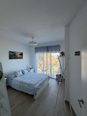 A bedroom with a bed, a nightstand, a lamp, a painting, a window with curtains, and a sign on the wall. - A&N Playa Madrid 1, Almayate (Vélez Málaga)
