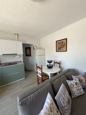 Een knus woongedeelte met een kitchenette, een eethoek en een bank met decoratieve kussens.