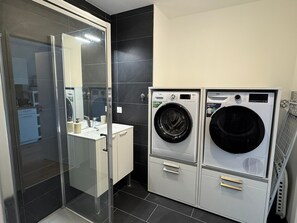 A modern bathroom with a glass shower enclosure, a sink, and two stacked front-loading washing machines. - Modern apartment, pets allowed - 4 guests (Dives-sur-Mer)