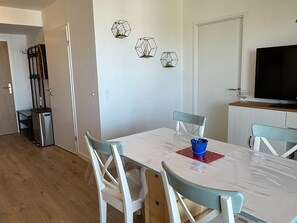 A dining area with a white table, blue chairs, and a TV on a wooden cabinet. - Modern apartment, pets allowed - 4 guests (Dives-sur-Mer)