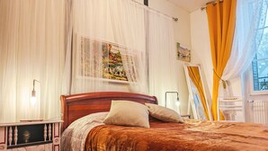 Ein Schlafzimmer mit einem hölzernen Bett, weißen Vorhängen und einem Fenster mit gelben Vorhängen.